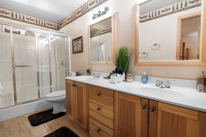 A bathroom with a glass shower enclosure, a toilet, a sink with a mirror, and wooden cabinets. - Sugarbear Cabin (Sugarloaf)