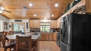 Een keuken met houten kasten, een zwarte koelkast en een eethoek met houten stoelen.