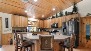 Een keuken met houten kastjes, een centraal eiland met barkrukken, roestvrijstalen apparatuur en een bord waarop 