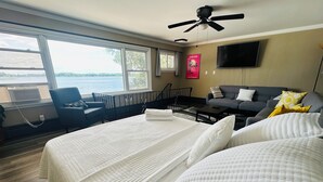 Hotellihuone, jossa on suuri sänky, sohva, televisio ja näkymä järvelle.