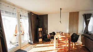 Een moderne woonkamer met een houten eettafel, zwarte stoelen, een open haard en een schuifpui naar een balkon.