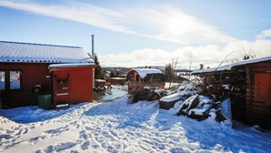 Een besneeud gebied buiten met een rood gebouw, een houten constructie en een klein vijvertje.