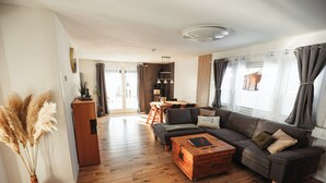 Een ruime woonkamer met een houten vloer, een donker leren bank, een houten salontafel en een eethoek op de achtergrond.