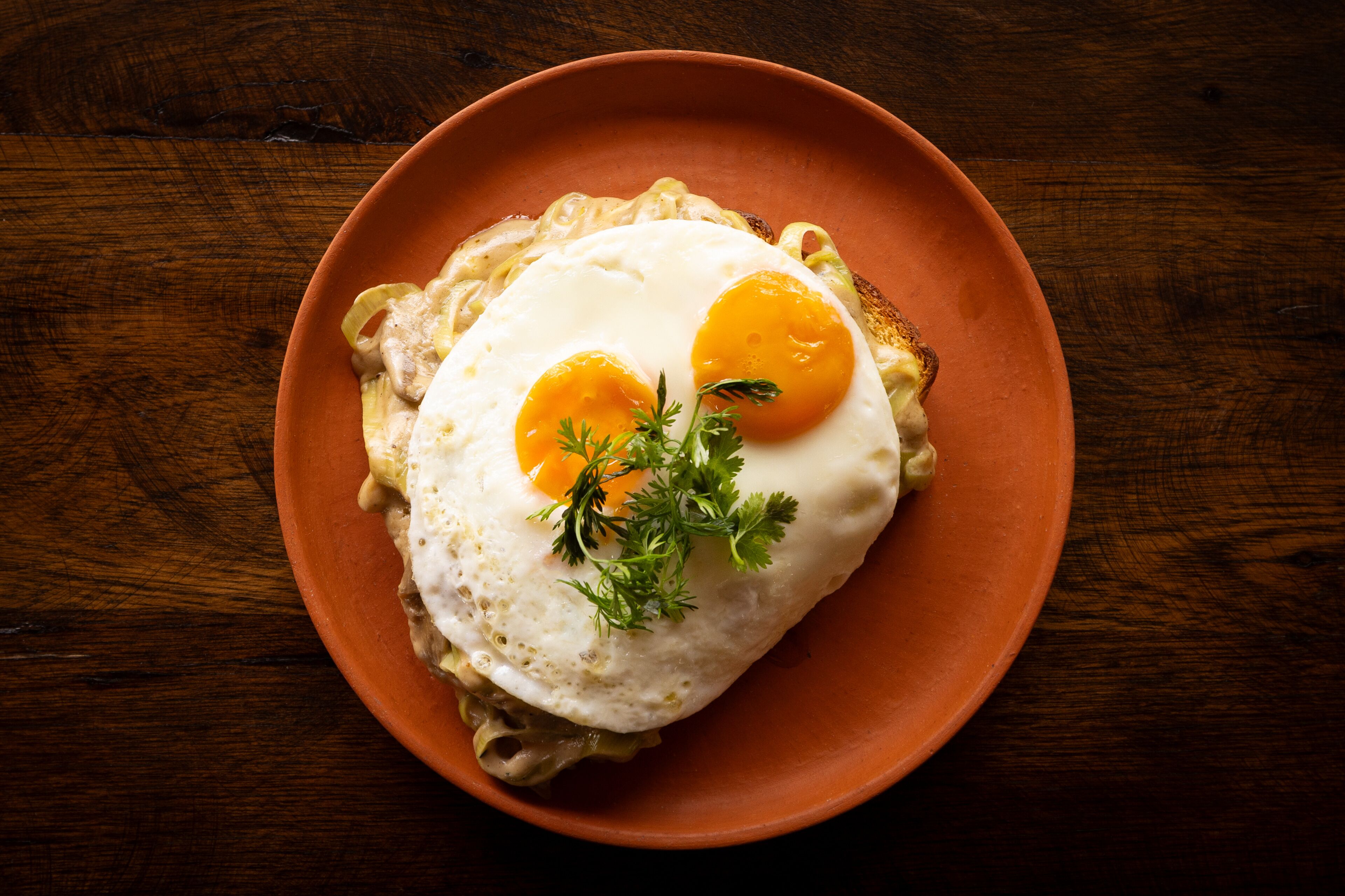 A plate with two sunny-side-up eggs on toast, garnished with parsley, on a brown plate.
