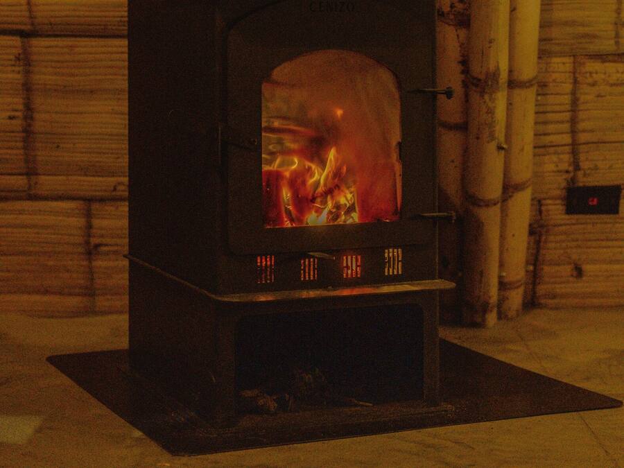 Una estufa de leña con fuego a la vista, frente a una pared de madera y una estructura de bambú a un lado.