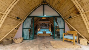 A cozy, triangular-roofed room with a bed, a wooden chair, and woven baskets. - Hotel Casa Selvaggio (Ráquira)