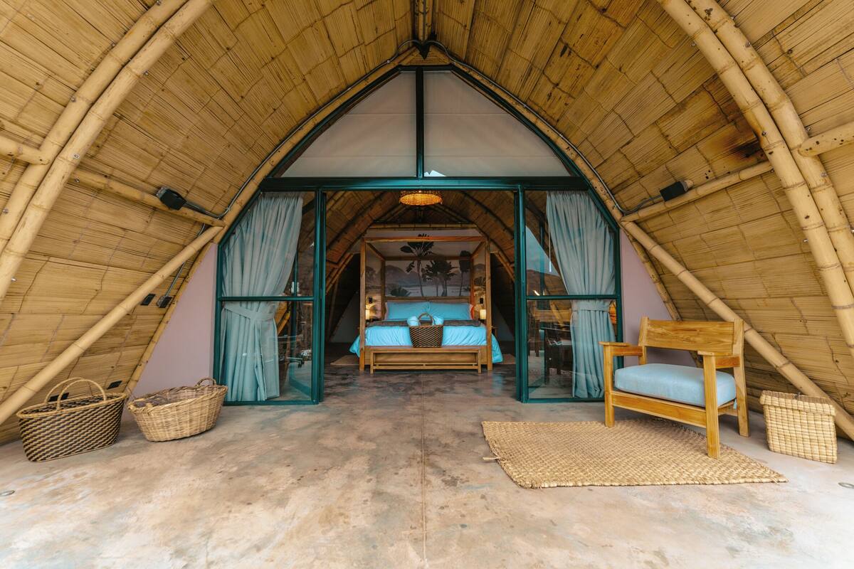 A cozy, triangular-roofed room with a bed, a wooden chair, and woven baskets.