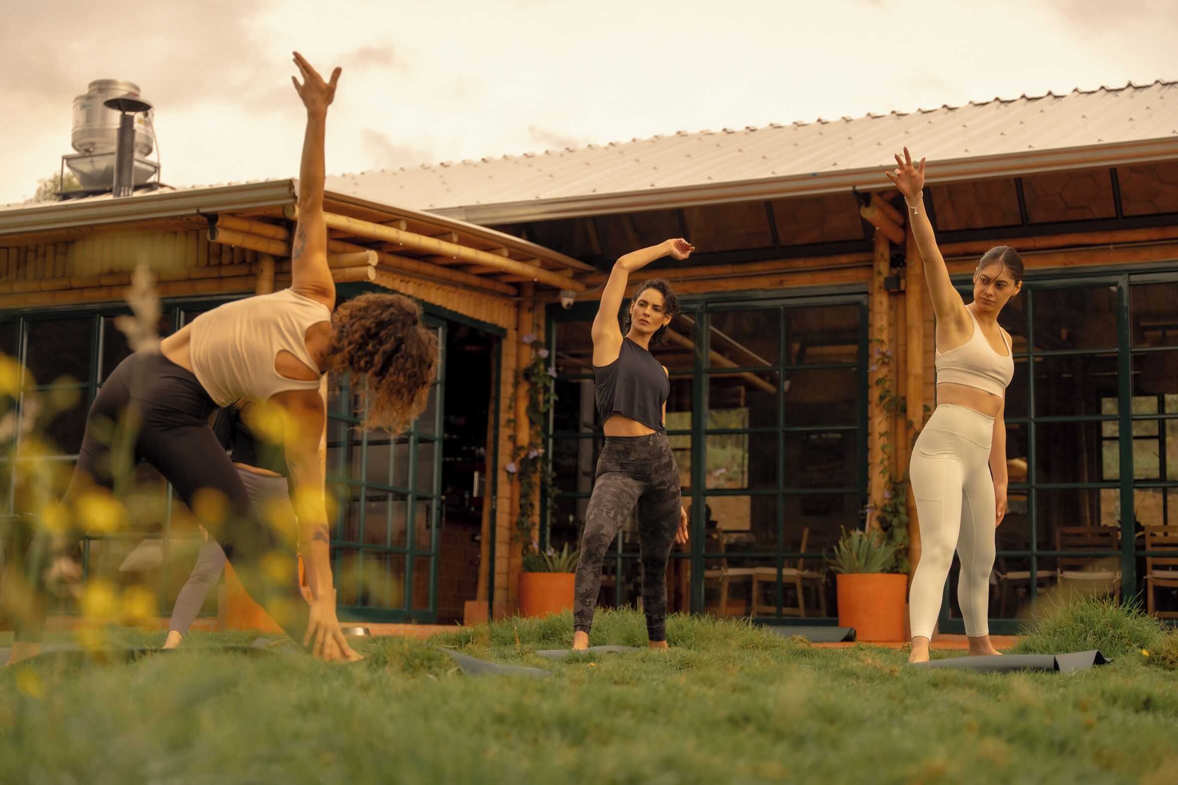 Three individuals practicing yoga outdoors in front of a rustic building with large windows and a metal roof.
