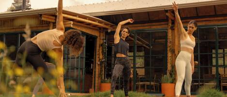 Three individuals practicing yoga outdoors in front of a rustic building with large windows and a metal roof.