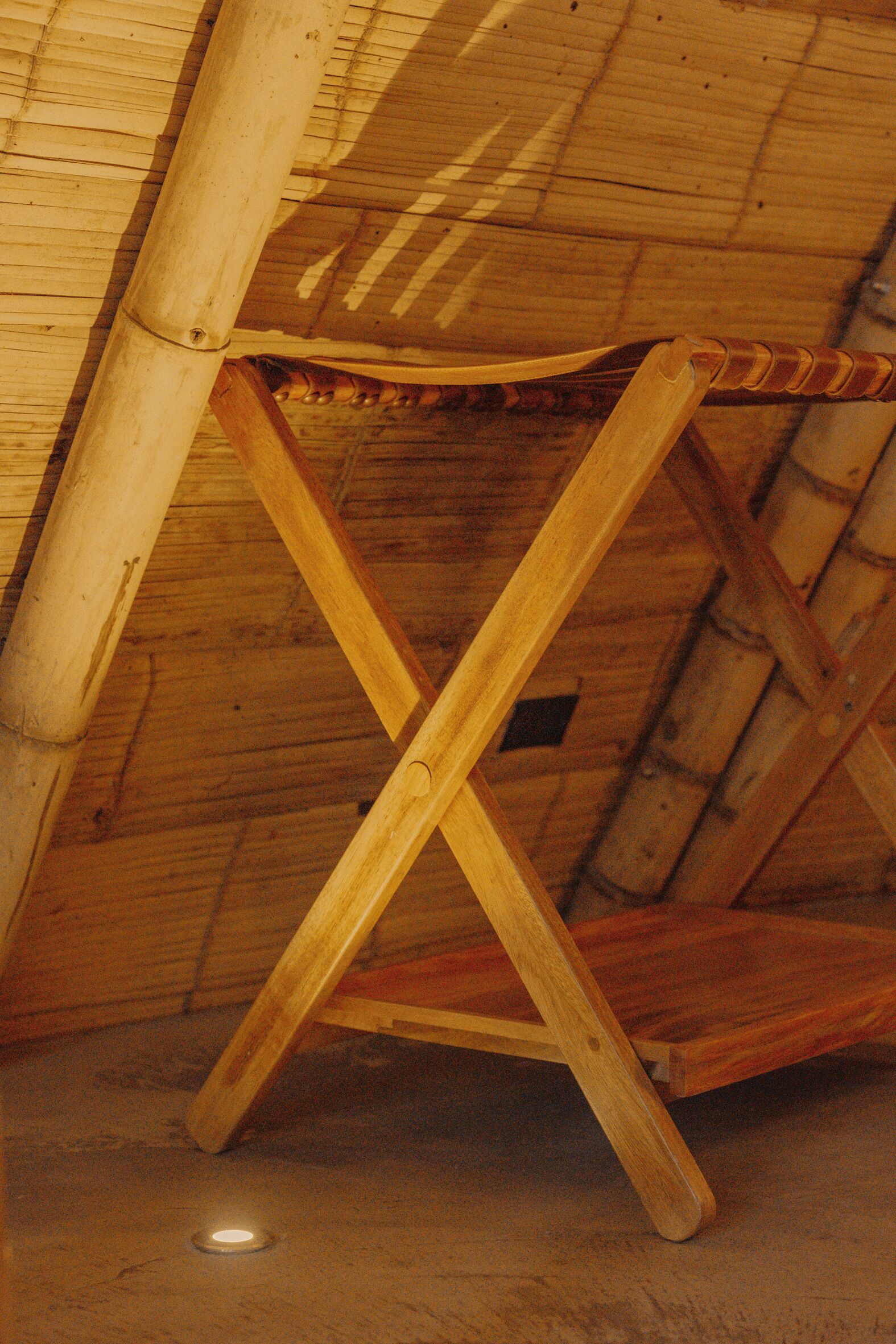 Una silla de madera con asiento y respaldo trenzados, ubicada bajo un techo inclinado con detalles de bambú.