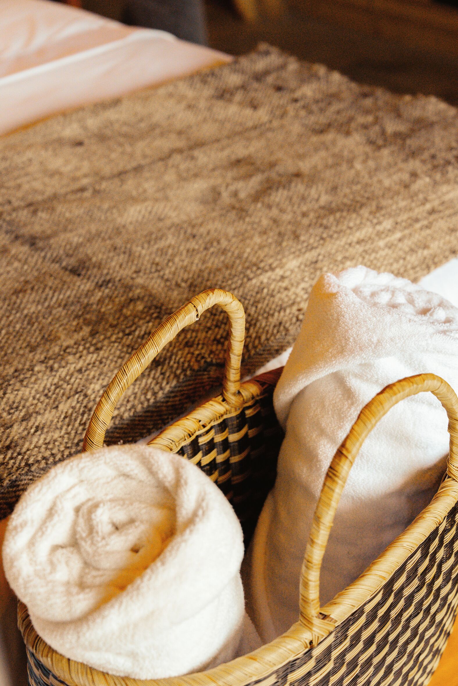 Un panier en osier contenant une serviette pliée et un oreiller, posés sur une surface en tissu texturé.