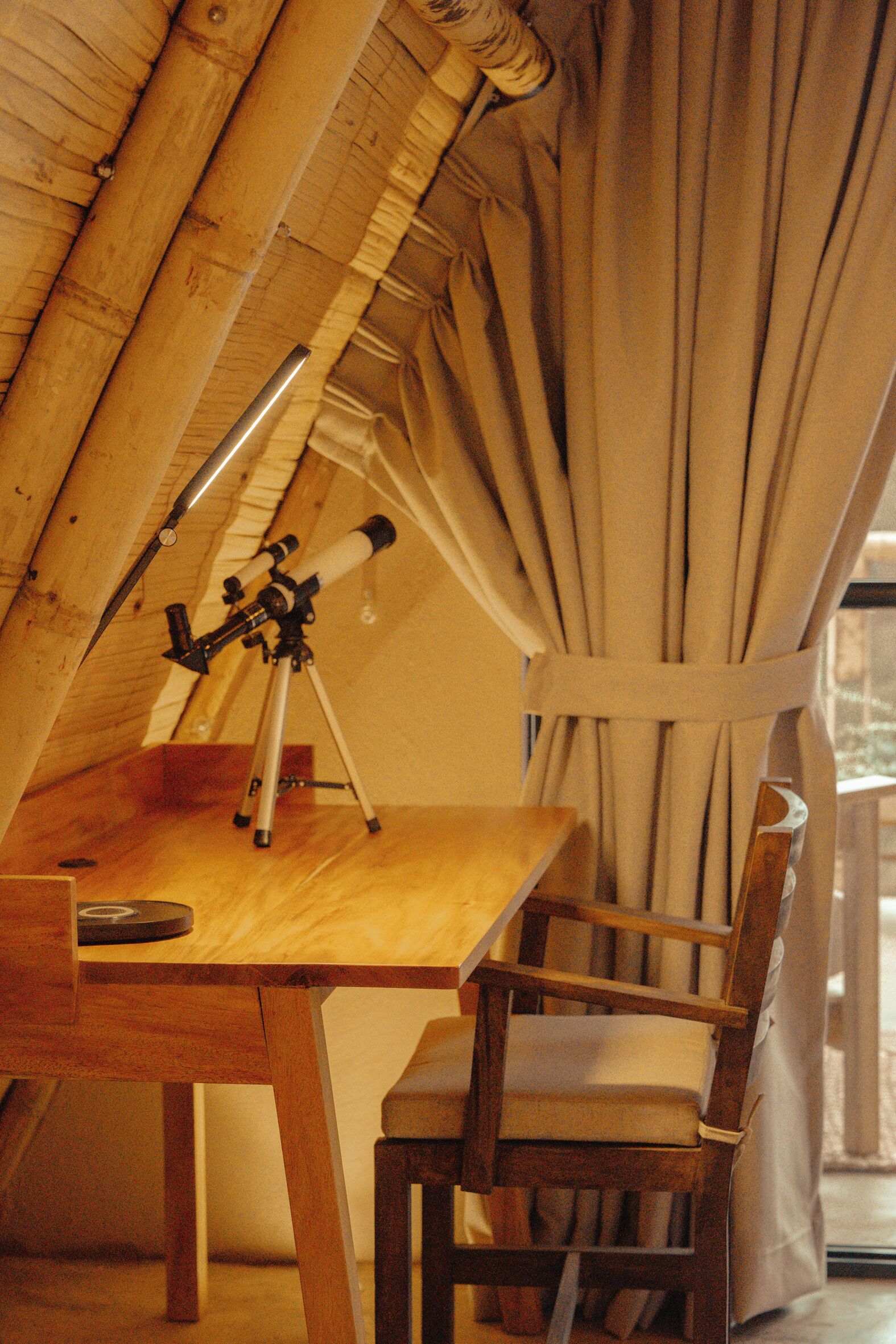 A wooden table with a telescope, a chair, and a window with curtains.