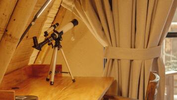 A wooden table with a telescope, a chair, and a window with curtains.