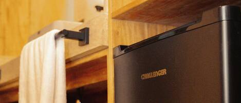 A compact black refrigerator with the brand name "CHALLENGER" in gold lettering, a wooden cabinet with a towel hanging on a metal hook, and a wooden countertop.