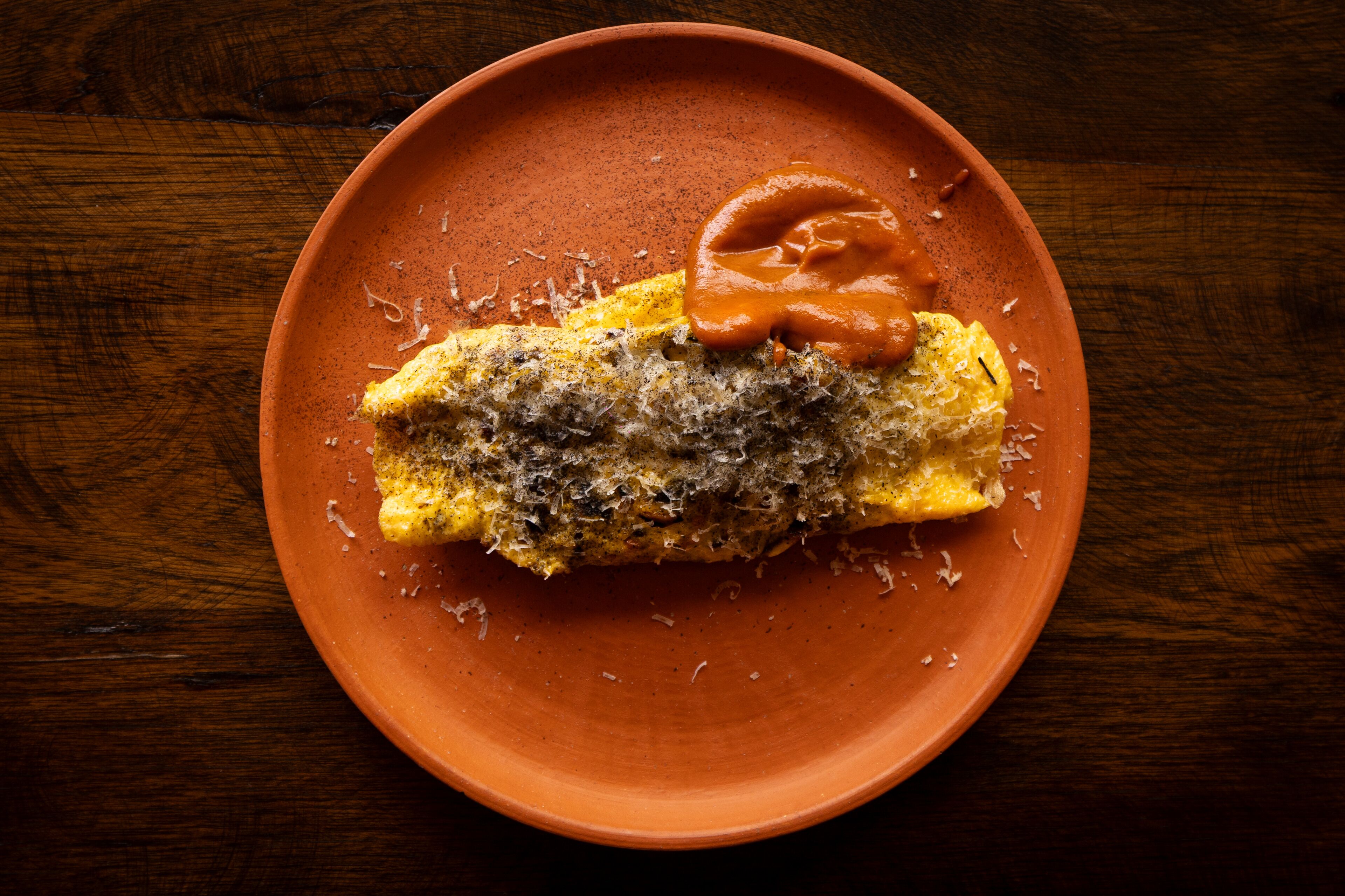 Un plato con una tortilla enrollada y una cucharada de salsa sobre una mesa de madera.