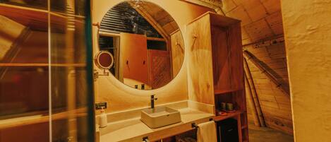 A wooden interior with a round mirror above a sink, wooden cabinets, and a towel rack.