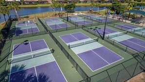 Un complejo de canchas de tenis con varias pistas, rodeado por una cerca, y un cuerpo de agua al fondo.
