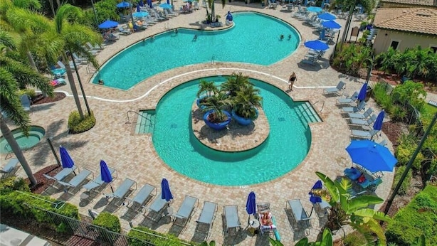 Una gran piscina de varios niveles con sillas de descanso y sombrillas, rodeada de palmeras y un edificio.
