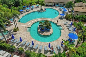 A large, multi-tiered swimming pool with lounge chairs and umbrellas, surrounded by palm trees and a building. - BRAND NEW TO THE RENTAL MARKET (Bradenton)