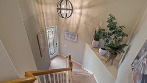 Un escalier avec une rampe en bois, un luminaire décoratif au plafond et des plantes en pot sur le palier.