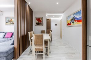 Een moderne woonkamer met een grijze bank, een eethoek met een witte tafel en stoelen, en een houten scheidingswand.