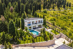 Ein modernes, zweistöckiges Haus mit Swimmingpool, umgeben von einer Steinmauer und üppiger Vegetation.