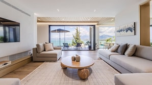 Un salon moderne doté d’un grand téléviseur, de deux canapés, d’une table basse et offrant une vue sur la mer grâce à de grandes fenêtres.