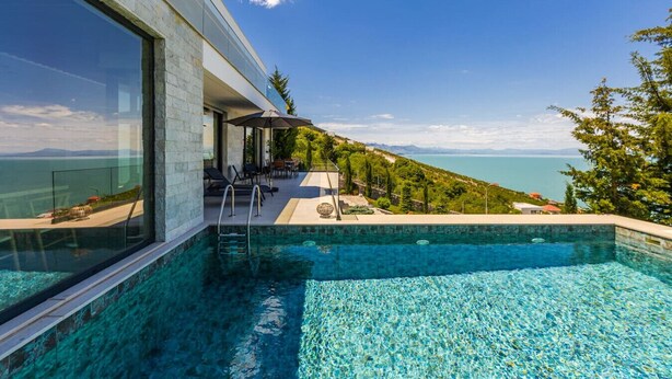 Une maison moderne avec une façade en verre, une piscine et une vue sur la mer.