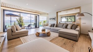 Un salon spacieux, doté d’un grand canapé, d’une table basse et offrant une vue sur un balcon avec une piscine.