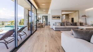 Un salon moderne doté d’un grand canapé, d’un coin repas et d’un mur de verre donnant sur une piscine.