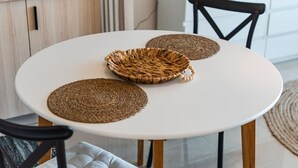 A round white table with three woven placemats and a woven basket. - Velipoja Beach Apartment by PikHost (Velipojë)