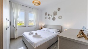 A modern bedroom with a large bed, a bedside table, and a view of the outdoors. - Velipoja Beach Apartment by PikHost (Velipojë)