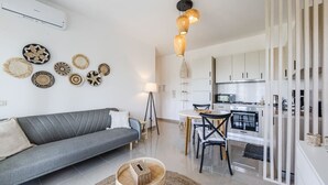 A modern living room with a grey sofa, a round coffee table, and a kitchen area with white cabinets and a microwave. - Velipoja Beach Apartment by PikHost (Velipojë)