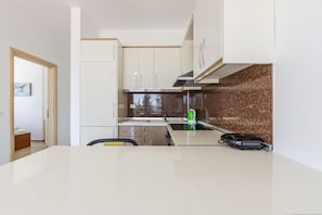A modern kitchen with white cabinets, a marble backsplash, and a dining area with a white table and chairs.