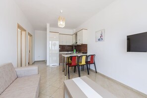 A modern apartment with a kitchenette, a dining area with colorful chairs, a sofa, and a flat-screen TV mounted on the wall.