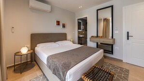 Et moderne hotelværelse med seng, sengebord, klimaanlæg og et badeværelse, der kan ses gennem en åben dør.