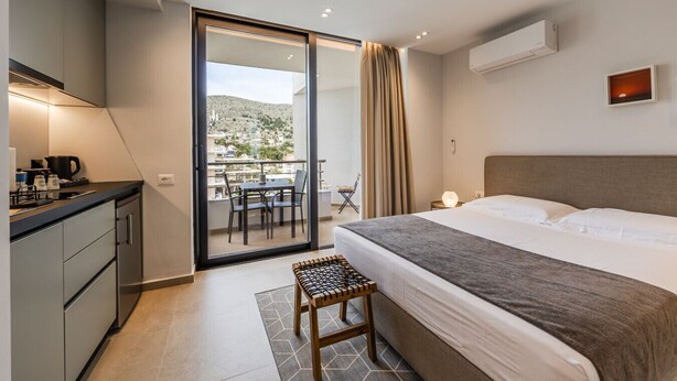 Et moderne hotelværelse med seng, et lille tekøkken, en balkon med bord og stole, samt udsigt over landskabet.