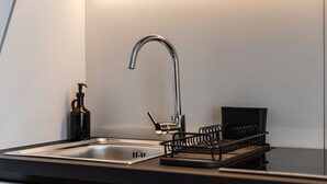 Et moderne køkken med en stålvask, en kromarmatur og en sort opvaskestativ.