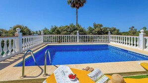 A pool with a white balustrade, a clear blue sky, and a palm tree in the background.