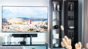 A modern living room with a flat-screen TV mounted on the wall, a grey sofa, a coffee table, and a decorative vase. - TOP Location-2BR Seafront&Steps to Ferry by ArcoCollection (Sliema)