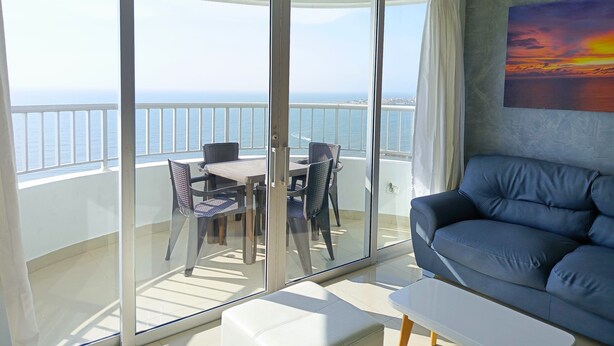 A balcony with a glass door, a dining table with chairs, and a blue sofa. - 2 Bedroom Oceanfront Apartment with Restaurant (Cartagena de Indias)
