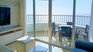 A balcony with a glass door, a TV mounted on the wall, and a seating area with chairs and a table. - 2 Bedroom Oceanfront Apartment with Restaurant (Cartagena de Indias)