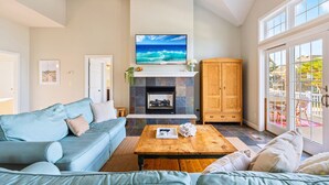 Een woonkamer met een stenen openhaard, een grote flatscreen-televisie, een houten kast en een blauwe bank.