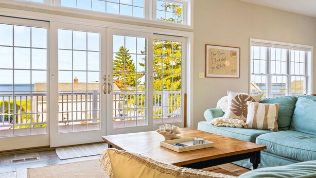Een ruime woonkamer met een grote schuifpui naar een balkon, een lichtblauwe bank en een houten salontafel.