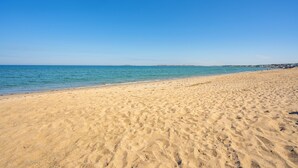 Een breed zandstrand met helderblauw water en een verre kustlijn.