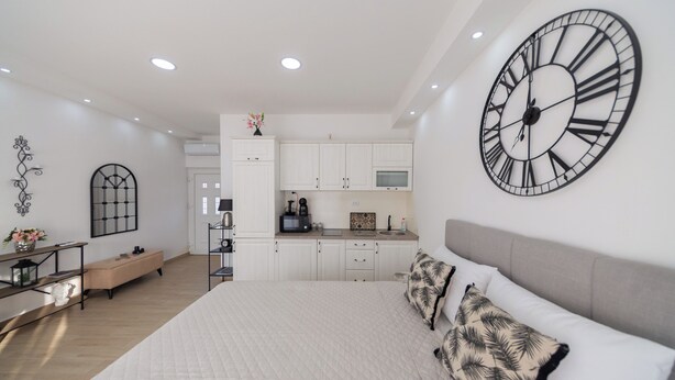 Un dormitorio moderno con una cama grande, un reloj de pared y una kitchenette al fondo.