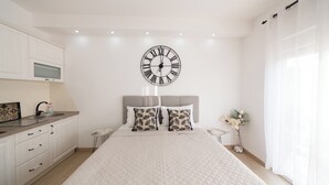 Un dormitorio con una cama grande, un reloj de pared, una mesita de noche y una ventana con cortinas.