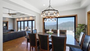 Une salle à manger spacieuse, dotée d’une grande table et de chaises, d’un lustre et offrant une vue sur les montagnes grâce à de larges fenêtres.