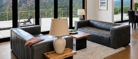 A modern living room with a leather sofa, a wooden coffee table, and a view of mountains through large windows.