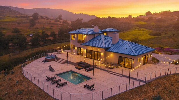 Une maison moderne dotée d’une piscine, d’un espace salon extérieur et offrant une vue panoramique sur les collines environnantes.